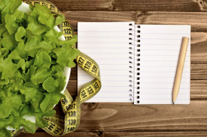 Empty notebook with vegetable salad on wooden table