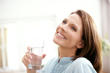 A mature woman looking pensive as she holds a glass of water