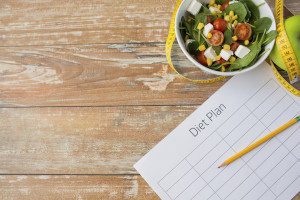 healthy eating, dieting, slimming and weigh loss concept - close up of diet plan paper green apple, measuring tape and salad